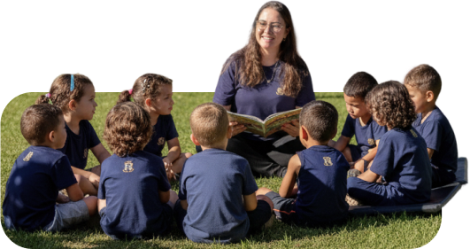 Professora lendo um livro em roda com as crianças no gramado